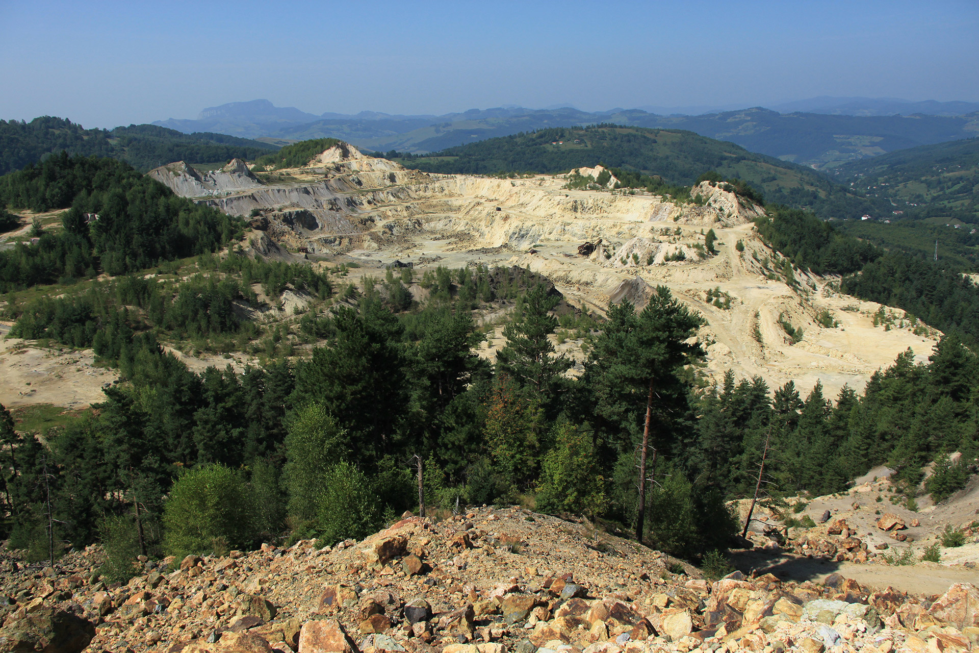 Et dagbrudd har gravd vekk en fjelltopp ved Roşia Montană. Grønn åskammer synes i bakgrunnen.