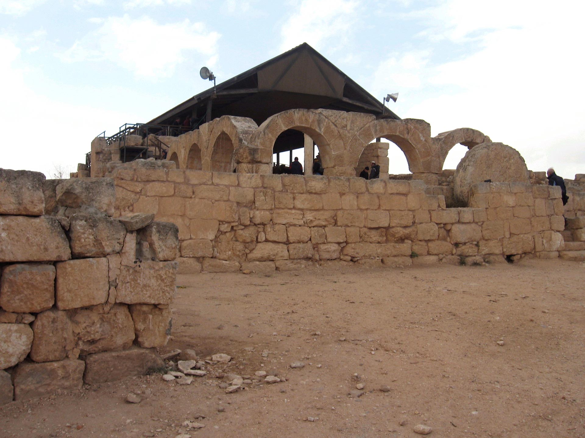 Ruiner med romerske buer i forkant av besøkssenteret til Susya-hulene. Turister kan skimtes på vei inn. 