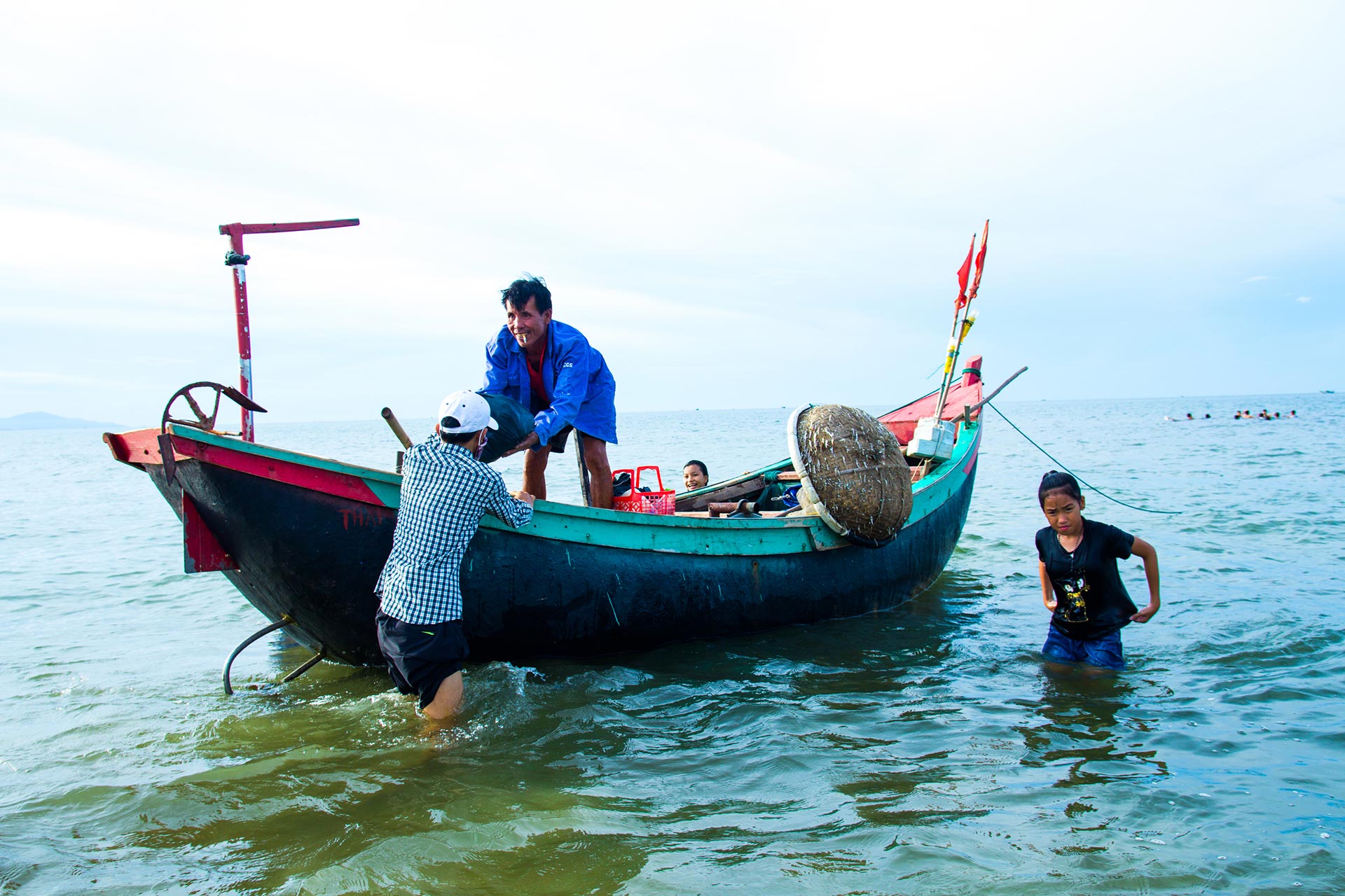  Fiskere i Hà Tĩnh. En eldre vietnamesisk fisker står i en båt og mottar en pose fra en yngre mann. To yngre jenter står i vannet ved siden av båten. 